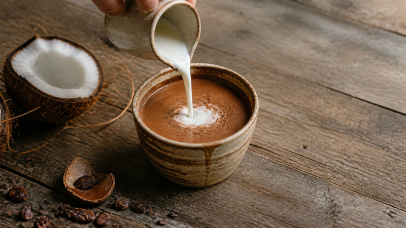 Coconut milk pouring into ceremonial cacao beside a cracked coconut